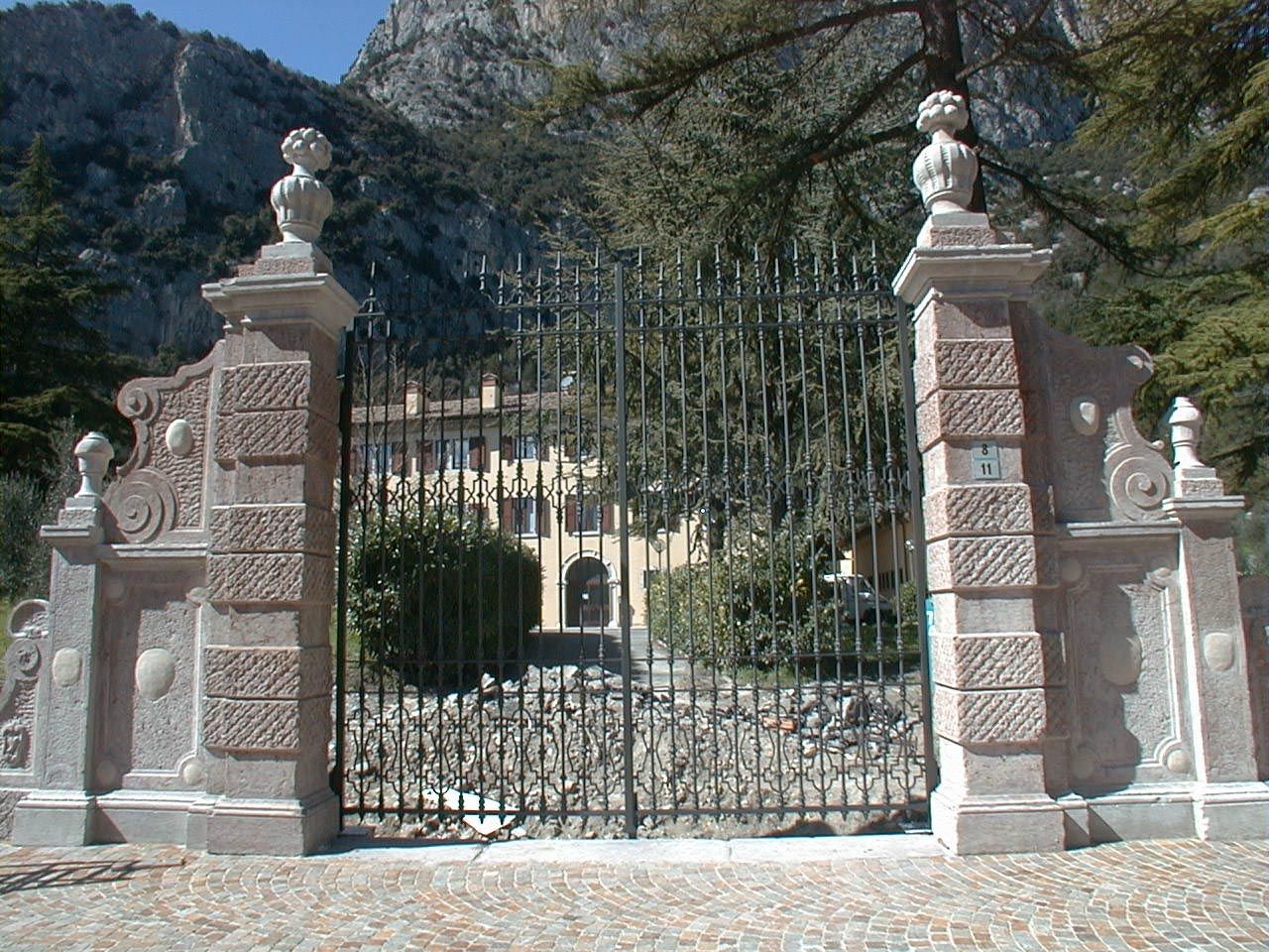 Cancello in ferro battuto tra pilastri in pietra decorati, con la montagna dietro