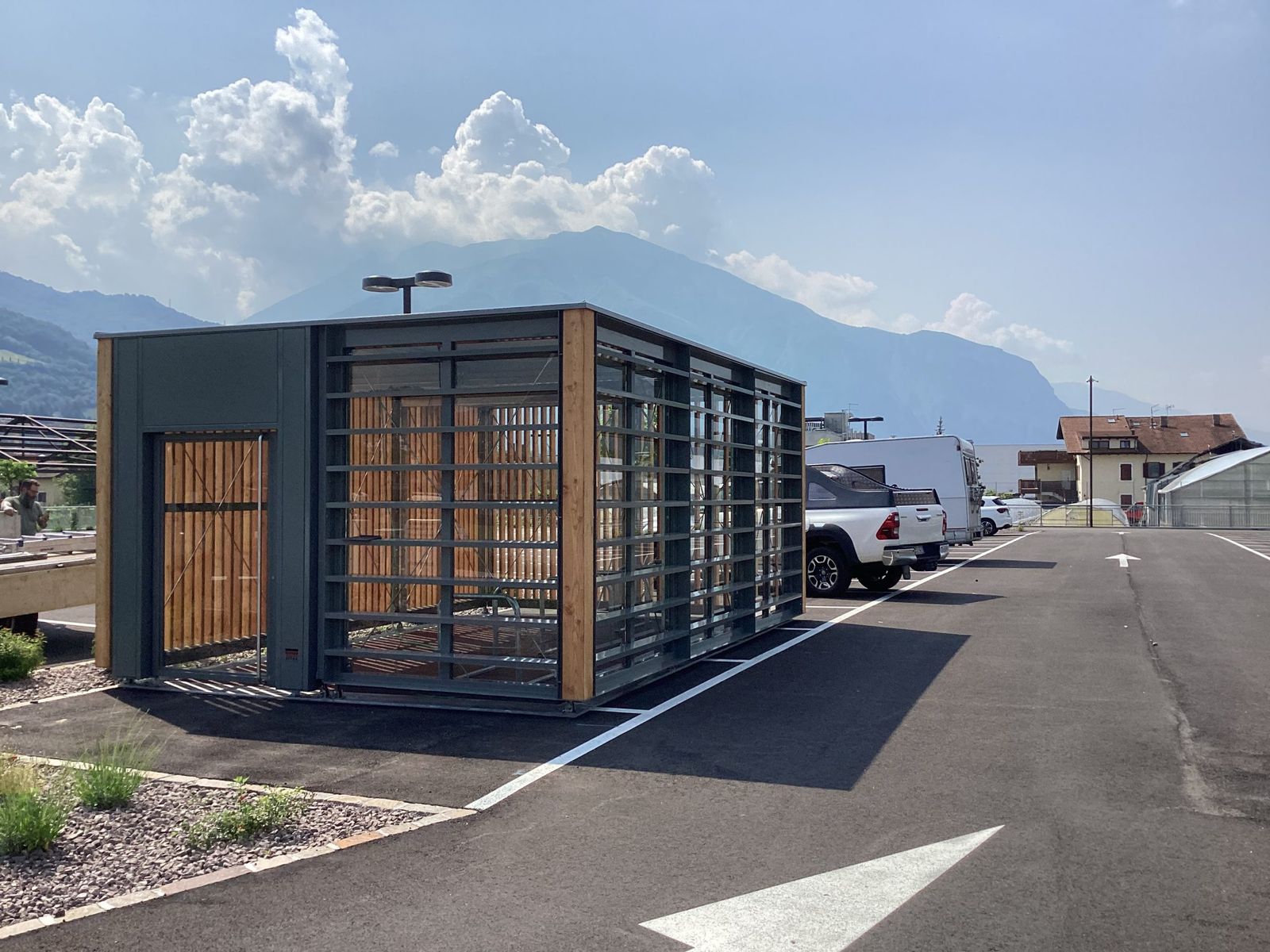 Box per biciclette con lamelle in legno e acciaio in un parcheggio, con le montagne dietro