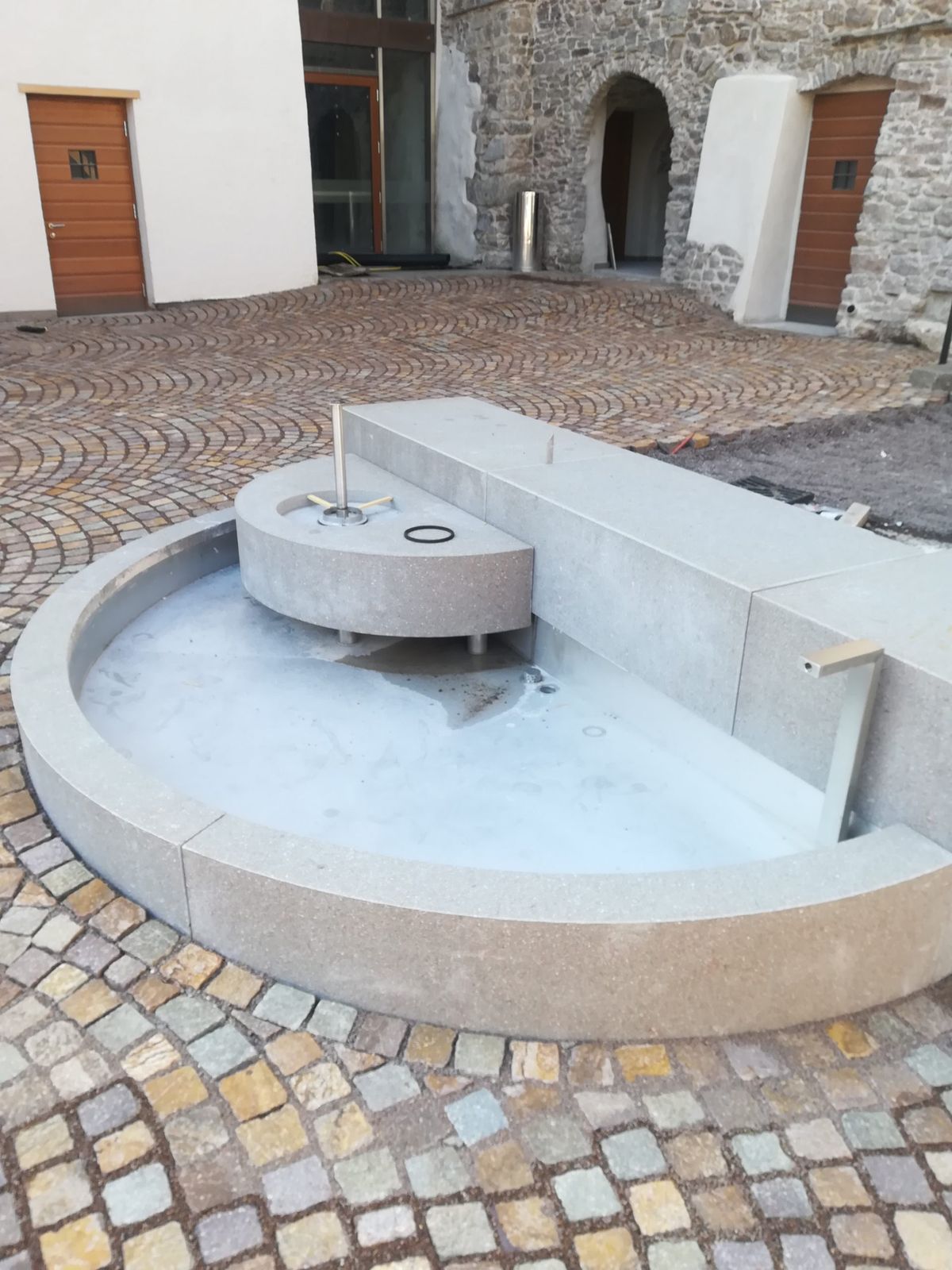 Fontana in pietra con vasca circolare in una corte pavimentata a ciottoli