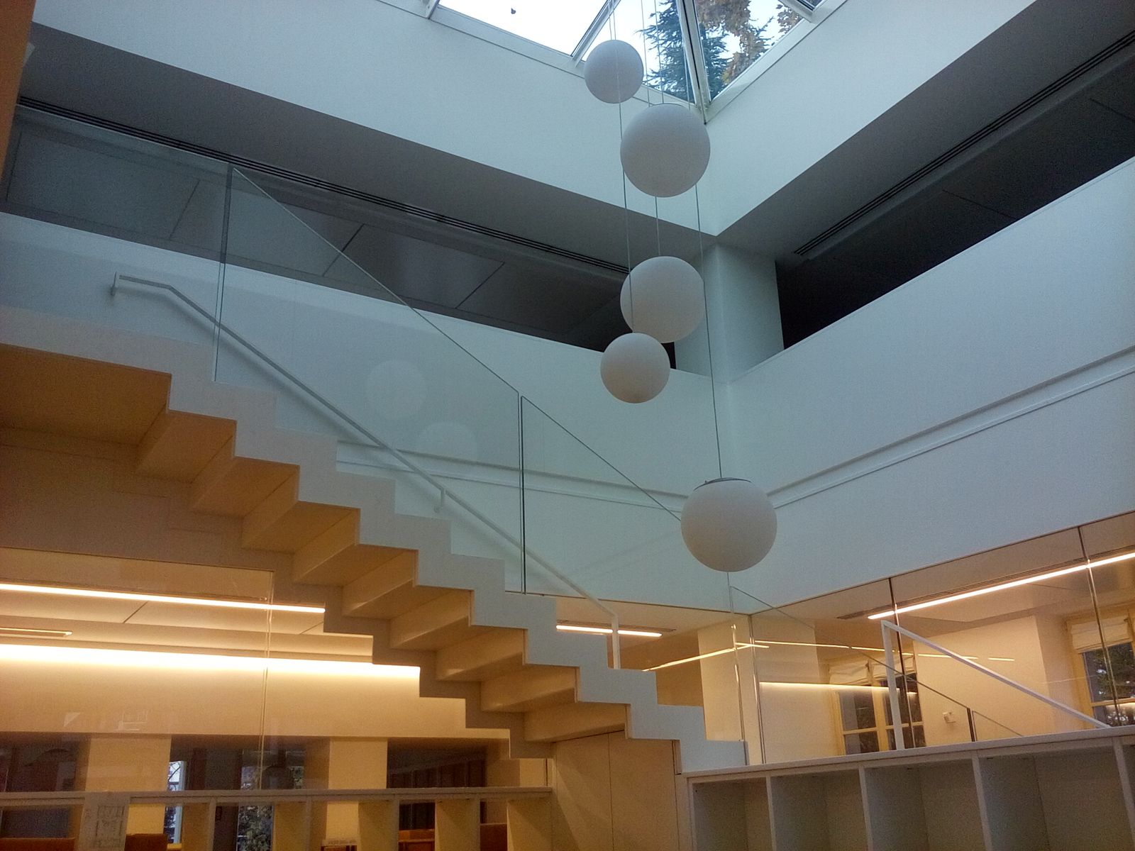 Scala sospesa con gradini e parapetto in vetro sotto il lucernario con le sfere luminose