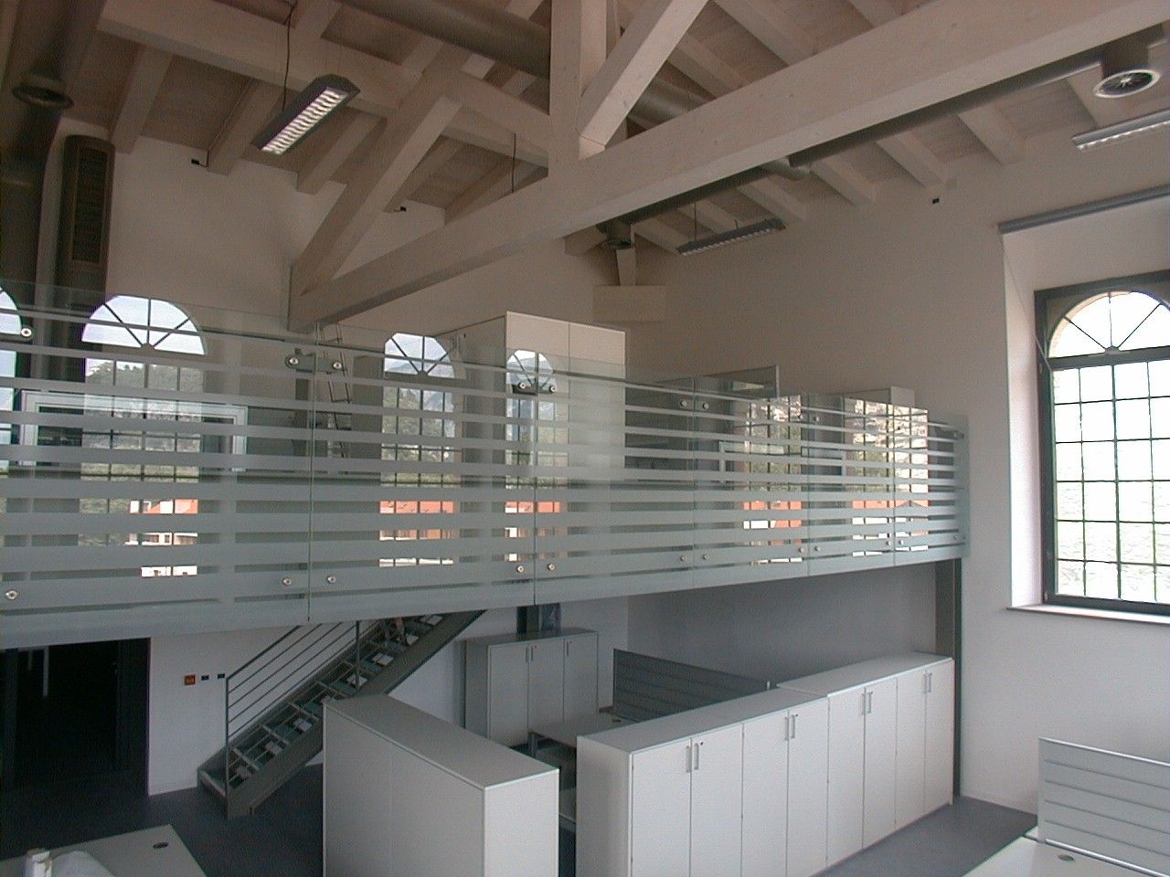Soppalco con parapetto in vetro e scala, sala con soffitto in legno e finestre ad arco